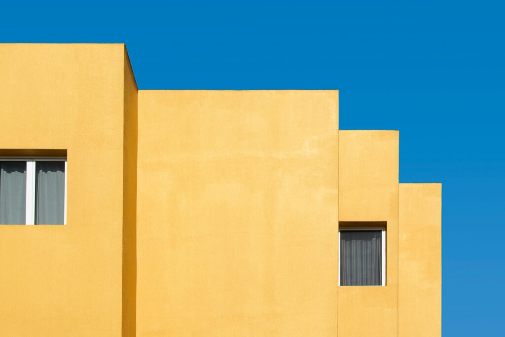 Minimalist yellow building facade with windows against a vivid blue sky.